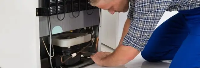 Refrigerator repair technician servicing the compressor and condenser area in Scottsdale, AZ