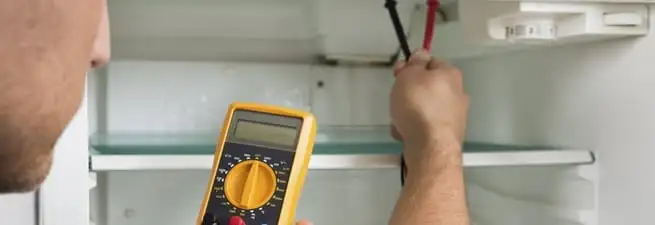 Refrigerator repair technician testing electrical components with a multimeter in Scottsdale, AZ