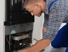 Refrigerator repair technician servicing the compressor and condenser area in Scottsdale, AZ